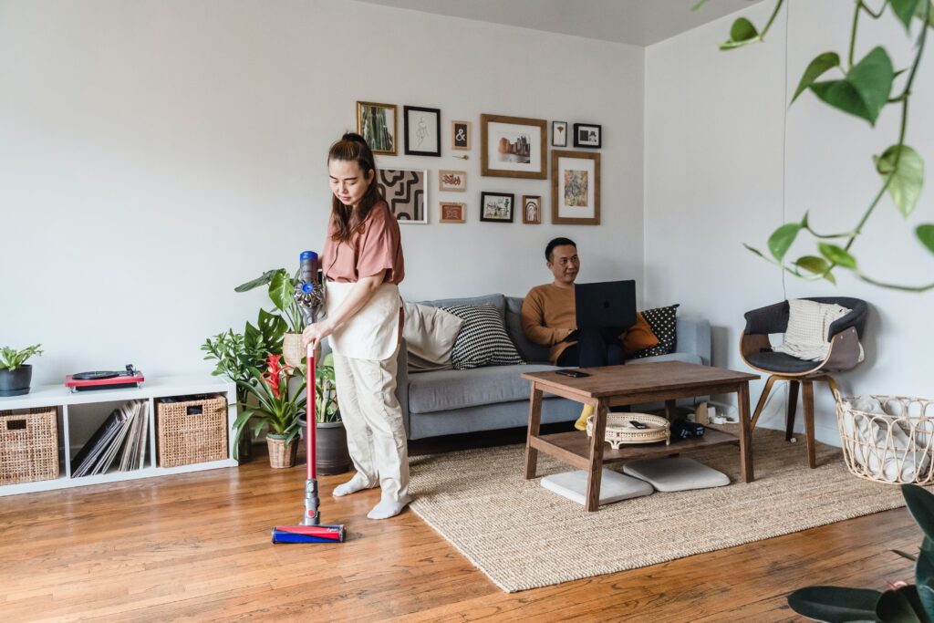 A woman cleaning the floor using a modern cordless Dyson vacuum cleaner. 